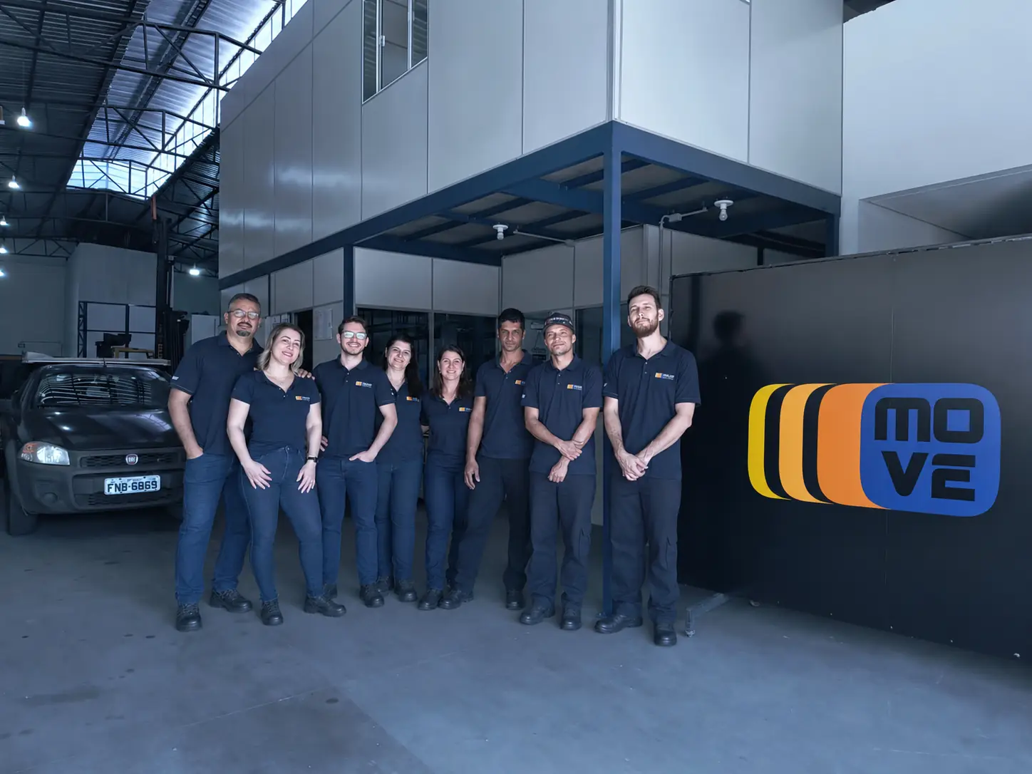 Equipe da Move Empilhadeiras reunida em frente ao painel com a marca, na sede em Marília